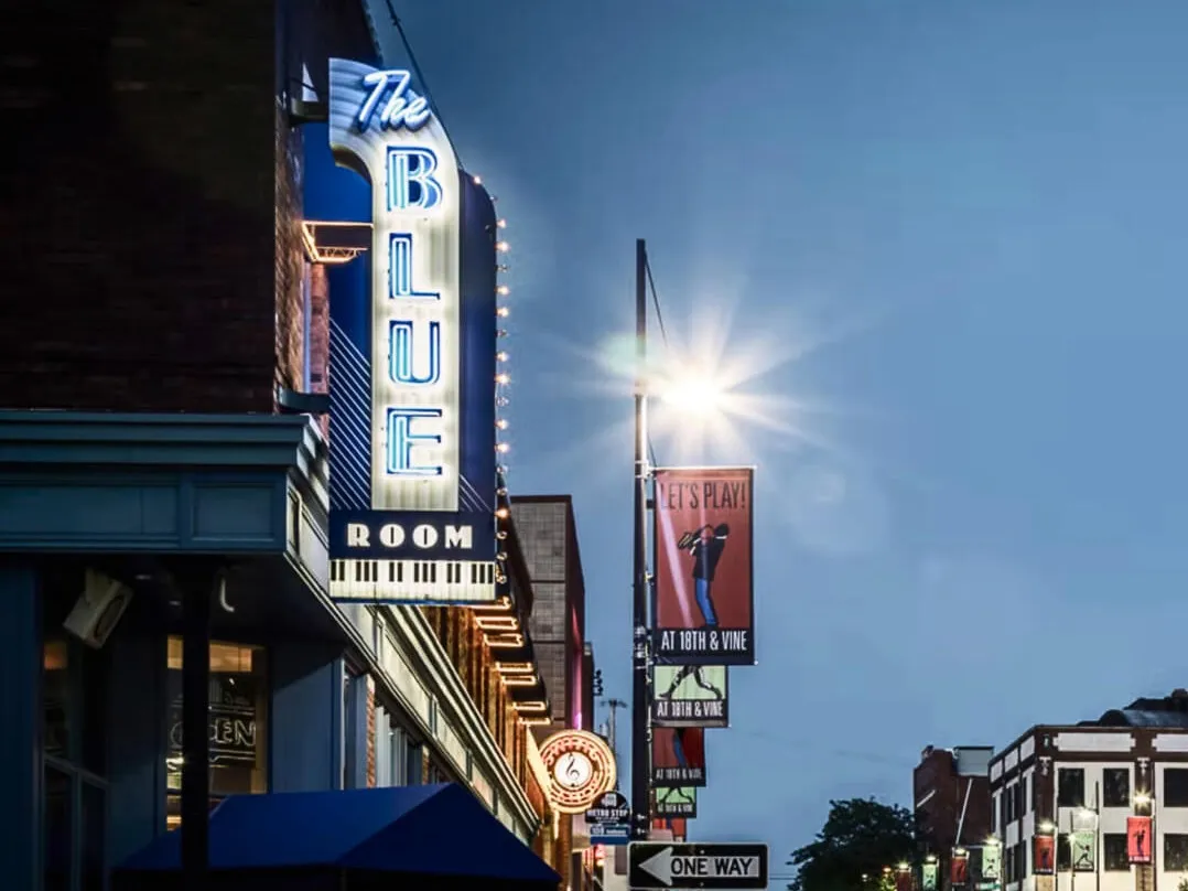 The Blue Room's neon sign lit at dusk on 18th Street, with an "At 18th & Vine" street banner beside it.